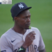Baseball player in a New York Yankees uniform and cap eating a green lollipop.