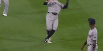 Baseball player in a gray uniform looking up to catch a baseball.