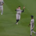 Baseball player in a gray uniform looking up to catch a baseball.