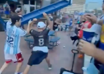 Two men fighting with a blue table over their heads in a crowd of people.