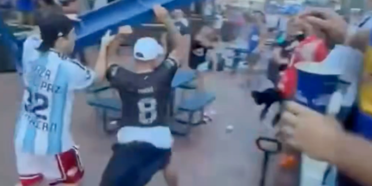 Two men fighting with a blue table over their heads in a crowd of people.
