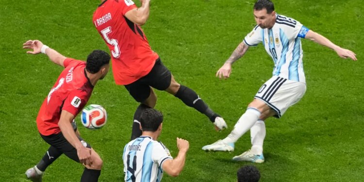 Lionel Messi takes a shot during a soccer match against an opposing team wearing red jerseys.