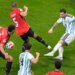 Lionel Messi takes a shot during a soccer match against an opposing team wearing red jerseys.