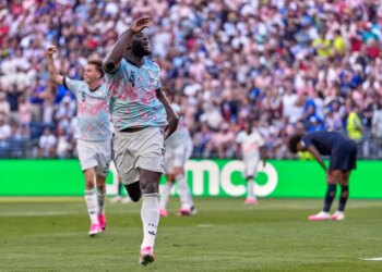 Belgium's Romelu Lukaku (9) celebrates his goal with his arms raised, while another player (5) raises his fist in the background, and an opposing player bends over in disappointment.