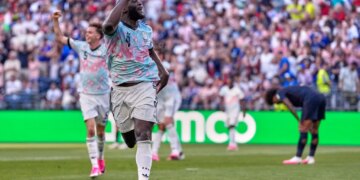 Belgium's Romelu Lukaku (9) celebrates his goal with his arms raised, while another player (5) raises his fist in the background, and an opposing player bends over in disappointment.