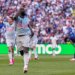 Belgium's Romelu Lukaku (9) celebrates his goal with his arms raised, while another player (5) raises his fist in the background, and an opposing player bends over in disappointment.