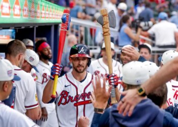 Atlanta Braves player Eli White celebrating a solo home run while holding a red baseball bat and a decorative axe in the dugout.