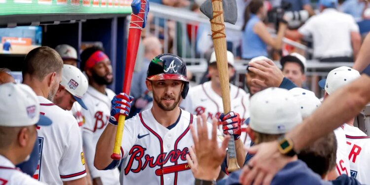 Atlanta Braves player Eli White celebrating a solo home run while holding a red baseball bat and a decorative axe in the dugout.