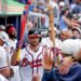 Atlanta Braves player Eli White celebrating a solo home run while holding a red baseball bat and a decorative axe in the dugout.