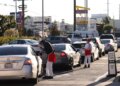 Workers in In-N-Out Burger uniforms take orders from a line of cars at a drive-through.