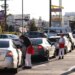Workers in In-N-Out Burger uniforms take orders from a line of cars at a drive-through.