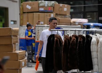 A vendor sweeps around fur clothing near a delivery pickup point at the Ritan International Trade Center, in Beijing, China, Tuesday, July 14, 2026.