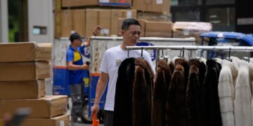 A vendor sweeps around fur clothing near a delivery pickup point at the Ritan International Trade Center, in Beijing, China, Tuesday, July 14, 2026.