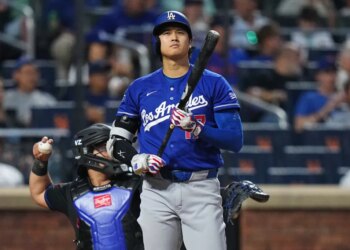 Shohei Ohtani at bat, wearing a blue Dodgers jersey and helmet, holding a bat, with a catcher behind him.