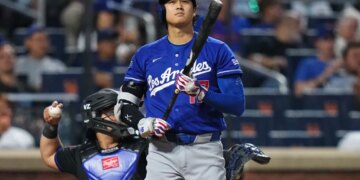 Shohei Ohtani at bat, wearing a blue Dodgers jersey and helmet, holding a bat, with a catcher behind him.