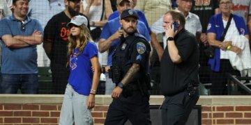 A fan is escorted off the field by police and security after entering the field during the ninth inning a baseball game between the Baltimore Orioles and the Chicago Cubs, Wednesday, July 8, 2026, in Baltimore.