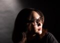 Senior reviewer Victoria Song wearing Meta Ray-Ban Display glasses while looking over her shoulder. The photo is lit so there are dramatic shadows across her face.