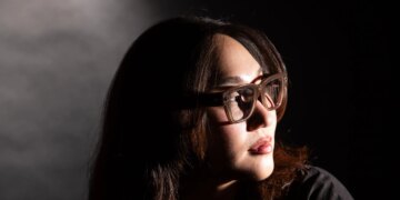 Senior reviewer Victoria Song wearing Meta Ray-Ban Display glasses while looking over her shoulder. The photo is lit so there are dramatic shadows across her face.