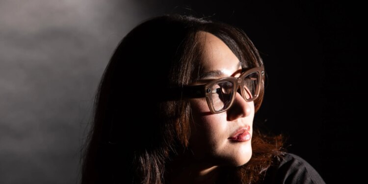 Senior reviewer Victoria Song wearing Meta Ray-Ban Display glasses while looking over her shoulder. The photo is lit so there are dramatic shadows across her face.