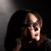 Senior reviewer Victoria Song wearing Meta Ray-Ban Display glasses while looking over her shoulder. The photo is lit so there are dramatic shadows across her face.