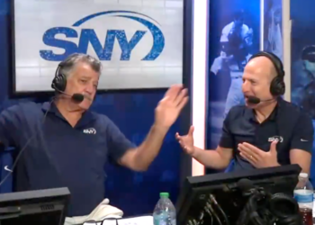 Two men in headphones and microphones, wearing blue SNY shirts, gesturing while broadcasting.