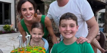 Family of four posing with a birthday cake that reads "BREXTON" in front of a building with a stone archway.