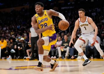 Basketball player Rui Hachimura in a Lakers uniform dribbles the ball downcourt while being guarded by Michael Porter Jr. in a Denver Nuggets uniform.