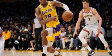 Basketball player Rui Hachimura in a Lakers uniform dribbles the ball downcourt while being guarded by Michael Porter Jr. in a Denver Nuggets uniform.