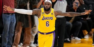 LeBron James in a yellow Lakers jersey with arms outstretched on a basketball court.