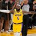 LeBron James in a yellow Lakers jersey with arms outstretched on a basketball court.