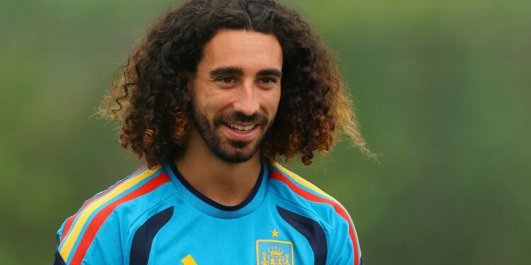 A smiling man with long curly hair and a beard wearing a blue and yellow soccer jersey.