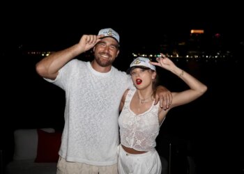 Travis Kelce and Taylor Swift wearing "Captain" and "First Mate" hats, respectively, with their arms around each other.