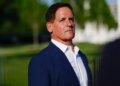 Mark Cuban, a white man with dark hair, wears a blue suit jacket and white shirt, looking forward and slightly to the right.