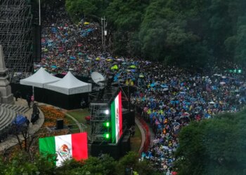 A large crowd of people with colorful umbrellas gathered, with large Mexican flags on display.