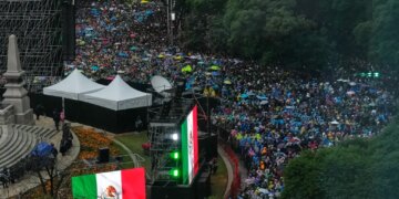 A large crowd of people with colorful umbrellas gathered, with large Mexican flags on display.