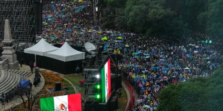 A large crowd of people with colorful umbrellas gathered, with large Mexican flags on display.