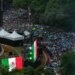 A large crowd of people with colorful umbrellas gathered, with large Mexican flags on display.