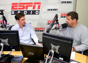Mike Greenberg and Mike Golic of ESPN Radio’s "Mike and Mike Show" sit at a desk with microphones and computers.