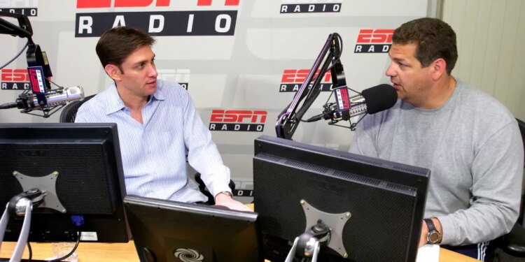 Mike Greenberg and Mike Golic of ESPN Radio’s "Mike and Mike Show" sit at a desk with microphones and computers.