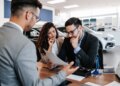 A salesman sitting across the table from a worried middle-aged couple in a car showroom.