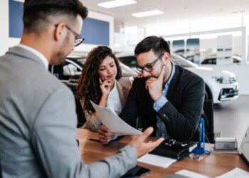 A salesman sitting across the table from a worried middle-aged couple in a car showroom.