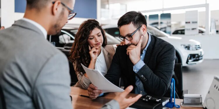 A salesman sitting across the table from a worried middle-aged couple in a car showroom.