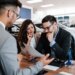 A salesman sitting across the table from a worried middle-aged couple in a car showroom.