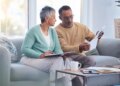 An elderly black couple discusses financial paperwork on a sofa.