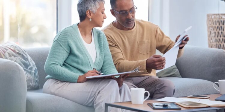 An elderly black couple discusses financial paperwork on a sofa.