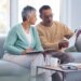 An elderly black couple discusses financial paperwork on a sofa.