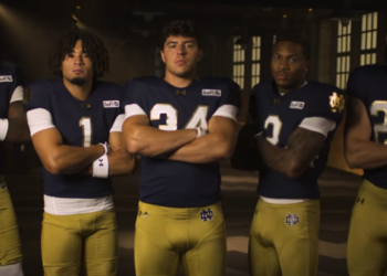 Five male football players in blue jerseys and gold pants stand with their arms crossed.