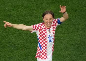 Luka Modric in a checkered red and white jersey on a green field.