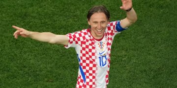 Luka Modric in a checkered red and white jersey on a green field.
