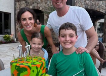 Family of four posing with a birthday cake that reads "BREXTON" in front of a building with a stone archway.